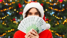 Frau mit Weihnachtsmütze hält Geldscheine vor ihr Gesicht.