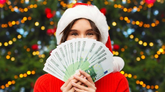 Frau mit Weihnachtsmütze hält Geldscheine vor ihr Gesicht.
